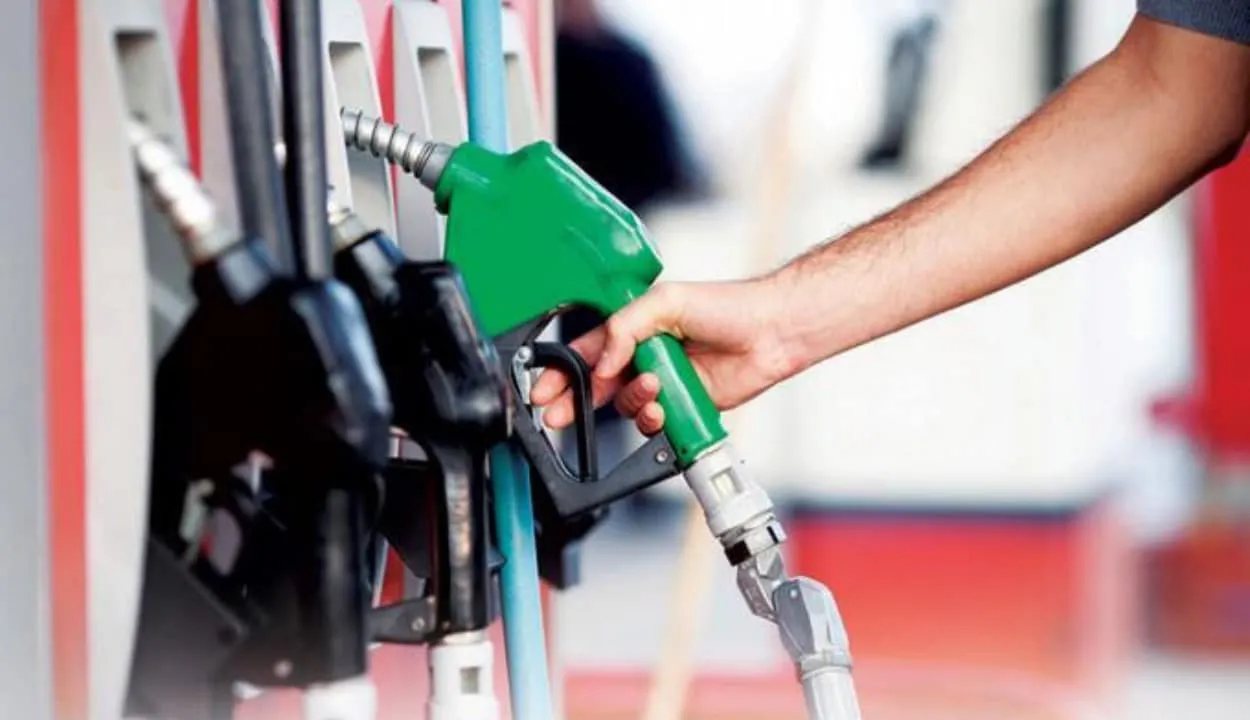 Person refueling a vehicle with a green gas pump nozzle at a gas station.