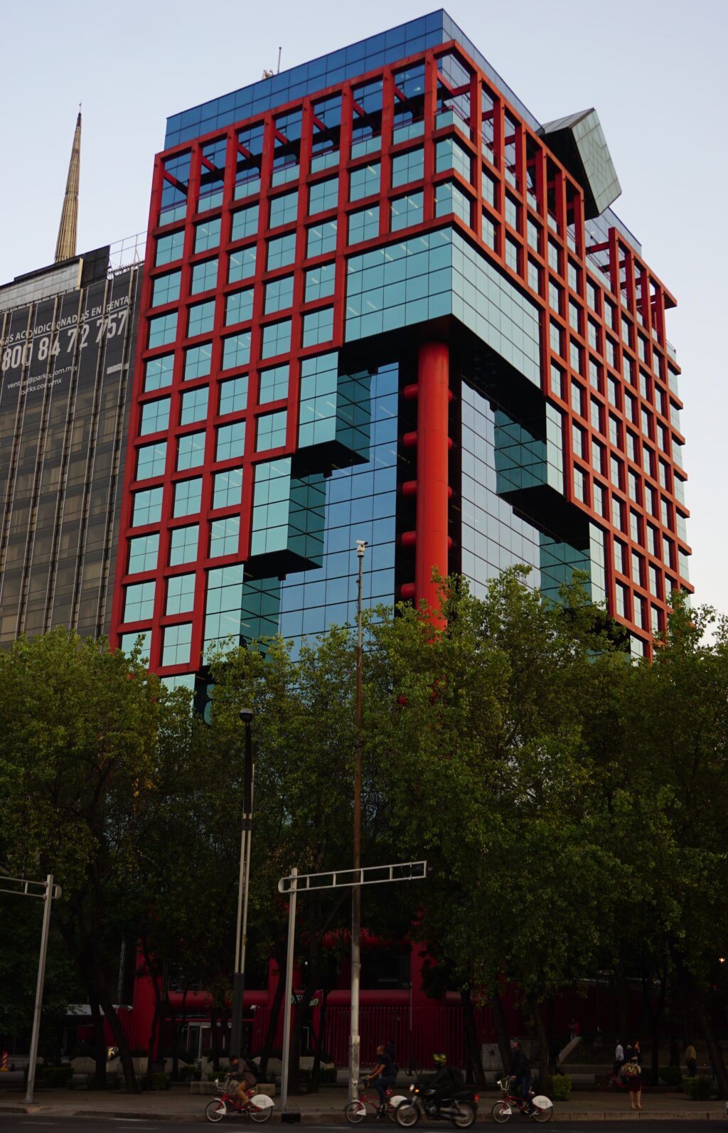 Edificio_CFE_at_Paseo_de_la_Reforma_164 - Petróleo y Energía Modern glass office building with a red lattice framework and blue-tinted windows rising above a tree-lined street.
