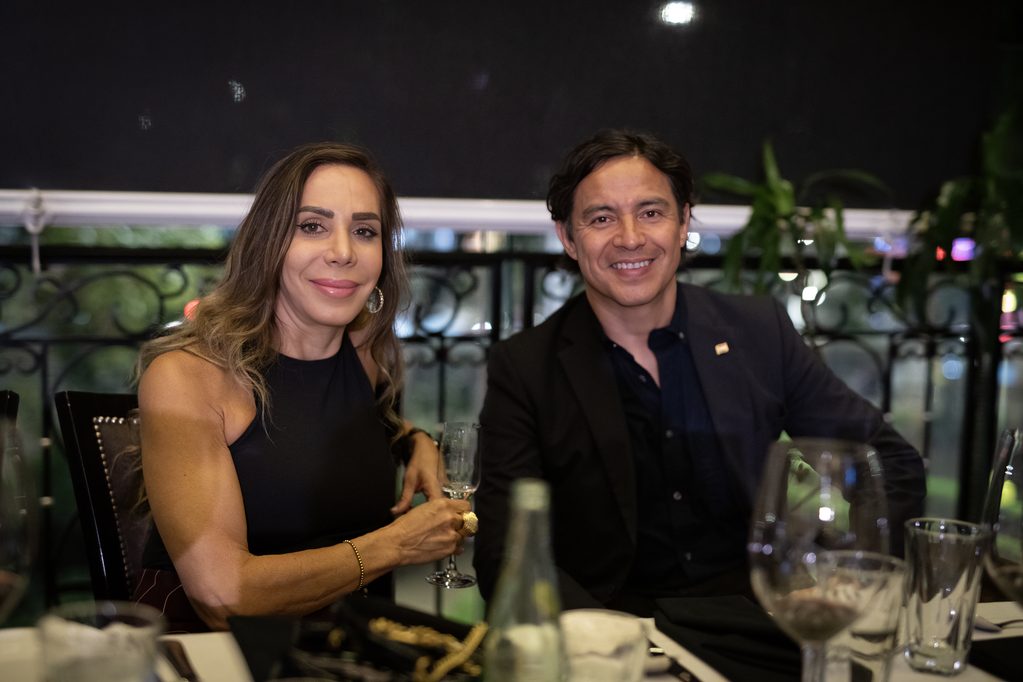 FLA_2568jpg - Petróleo y Energía Smiling man and woman in formal attire sit at a restaurant table with wine glasses in front of them.