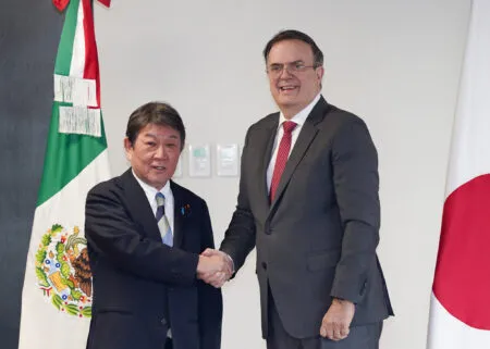 Two men in dark suits shake hands in front of national flags during a formal ceremony or photo op.