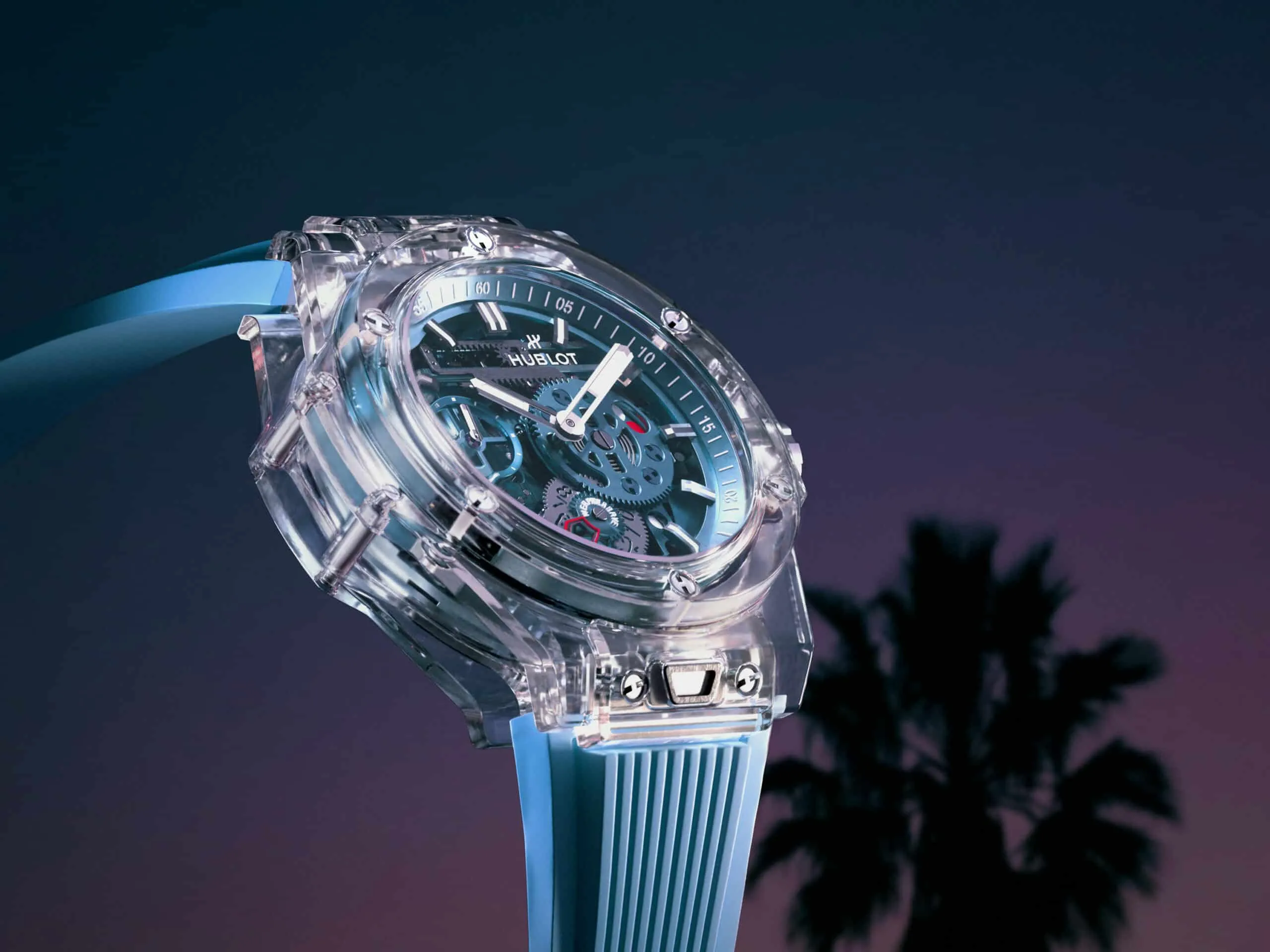 Transparent skeleton wristwatch with a blue strap displayed against a twilight sky backdrop.