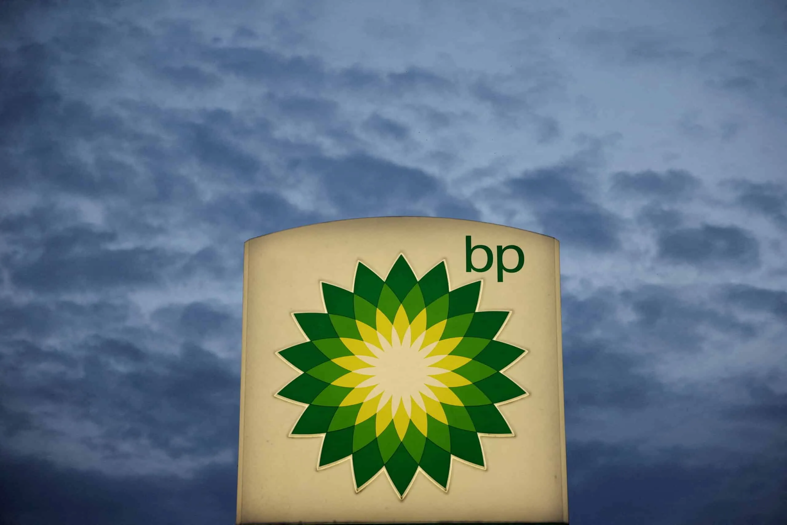 BP logo on a beige sign with a green and yellow sunburst, cloudy sky behind a
