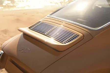 Close-up of a tan luxury car rear with chrome vents and Louis Vuitton branding, sun glare on the trunk lid