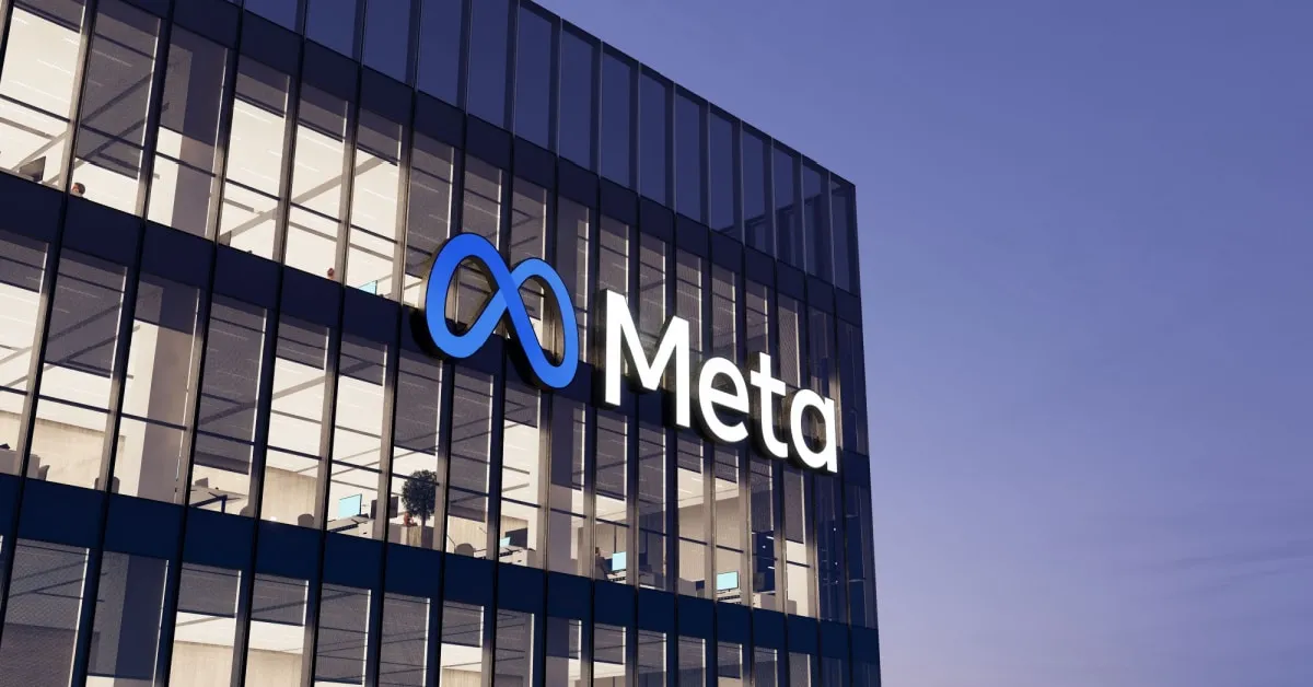 Glass office building with a blue Meta logo featuring an infinity symbol against a clear blue sky (logo on glass facade).