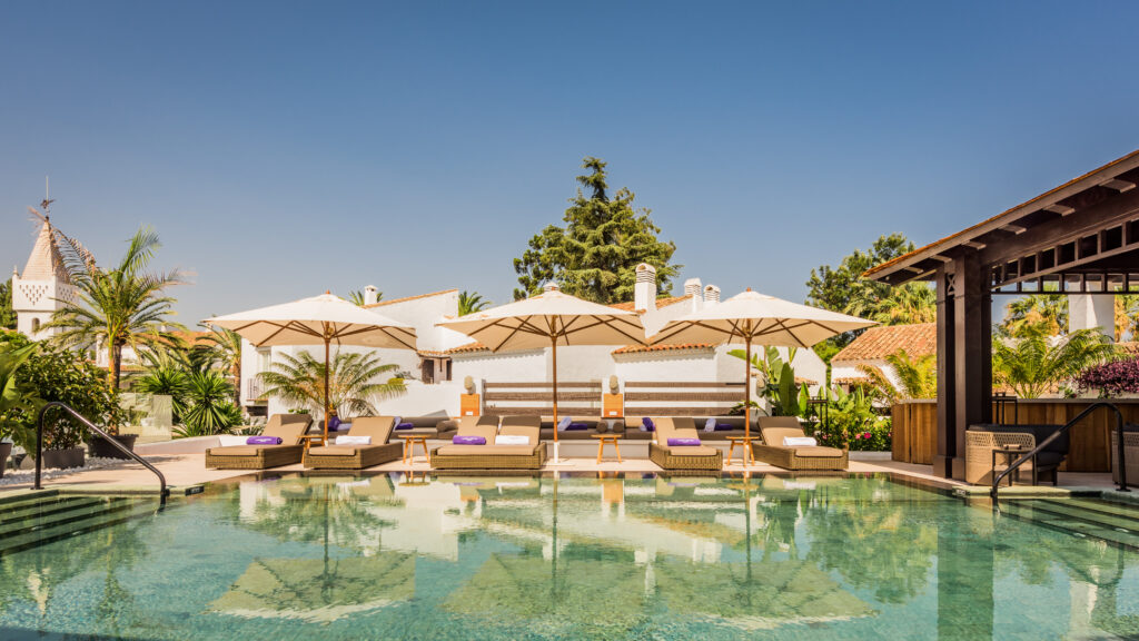 Nobu_Pool-4 - Petróleo y Energía Poolside lounge area with beige sunbeds under white umbrellas at a sunny resort setting with palm trees in the background