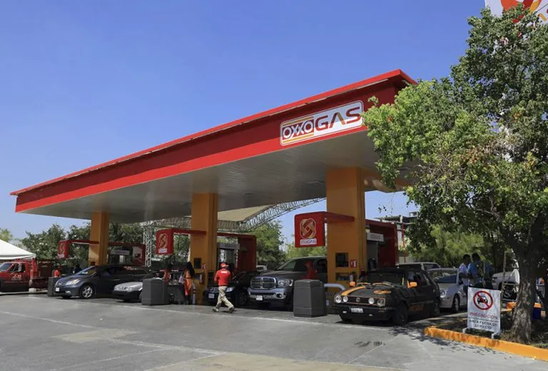 Oxogas gas station with a red canopy and orange pillars, cars at the pumps under a clear blue sky.
