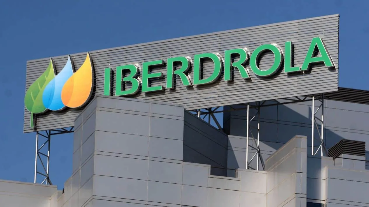 Iberdrola corporate sign with green letters and a multicolored leaf logo on a modern building against a clear blue sky.