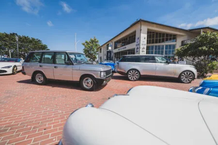 Several luxury cars parked on a brick plaza in front of a museum on a sunny day with a clear blue sky.