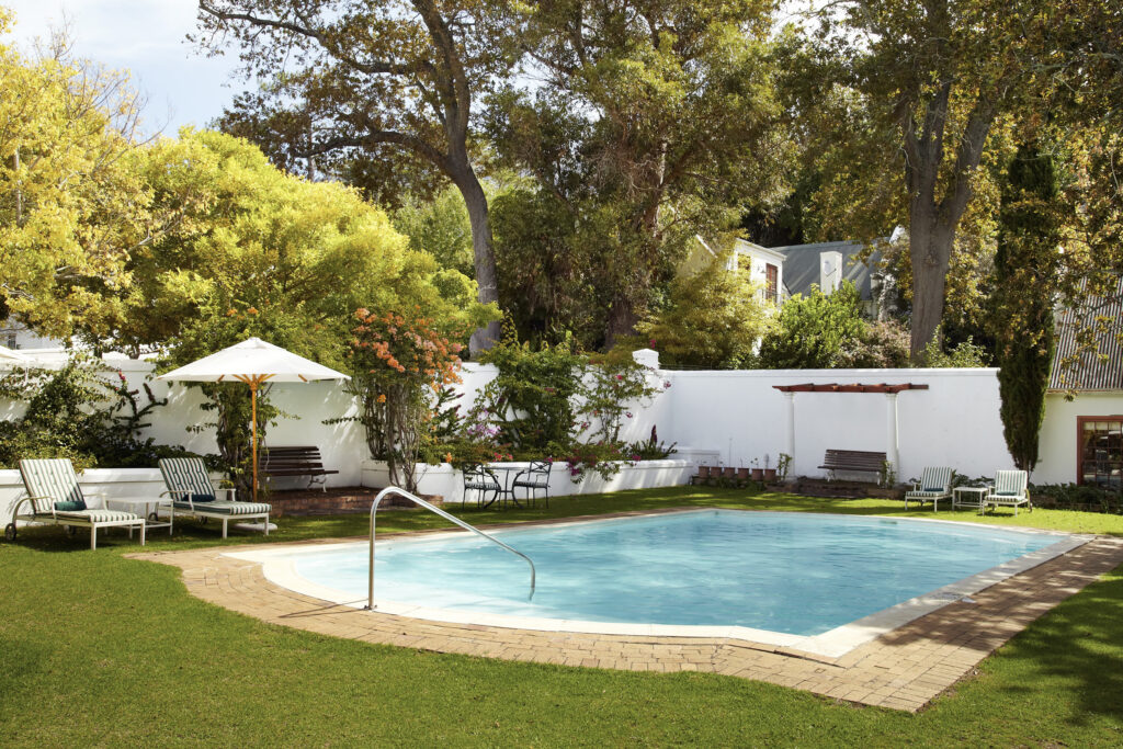 - Petróleo y Energía Backyard pool area with lounge chairs under a white umbrella and a grassy lawn surrounded by trees and a white wall fence