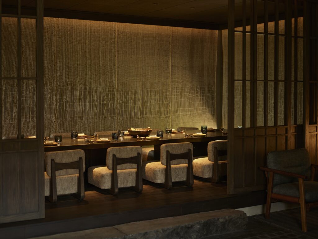 Toppu 5 - Petróleo y Energía Dimly lit dining area with a long wooden table set for a meal, beige cushioned chairs, and wooden lattice partitions across the room.