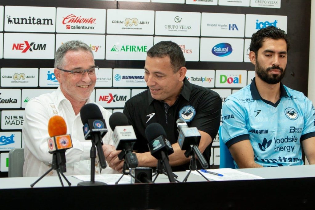 WhatsApp Image 2026-08-26 at 23647 PM 1 - Petróleo y Energía Three men at a press conference behind a sponsor backdrop, microphones in front of them (left in white shirt, center in black polo, right in blue sports jersey).
