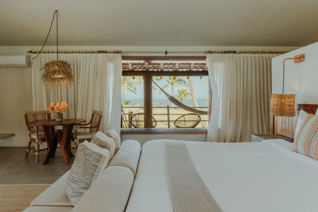 - Petróleo y Energía Bright tropical living room with white sofas, wicker pendant lamp, and a wooden dining set facing a balcony with palm trees and ocean view