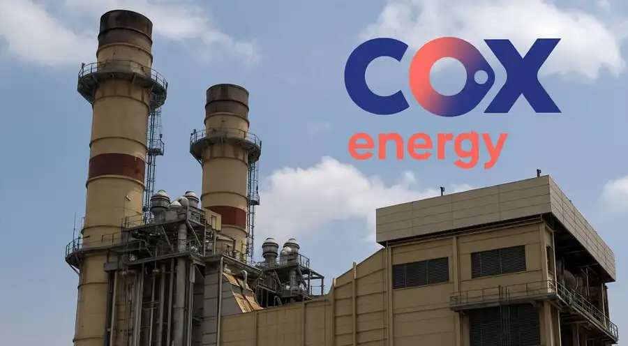 Industrial power plant with tall smokestacks and beige building, featuring the COX energy logo in the sky above.