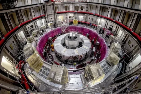 Interior of a large scientific reactor/particle accelerator chamber, with a central cylindrical core surrounded by a purple circular ring and metal scaffolding.