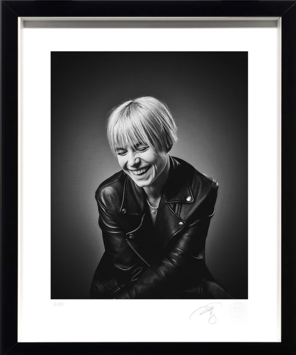 La actriz Jessie Buckley - Petróleo y Energía Black-and-white portrait of a smiling woman with short blonde hair, wearing a leather jacket, framed as wall art.
