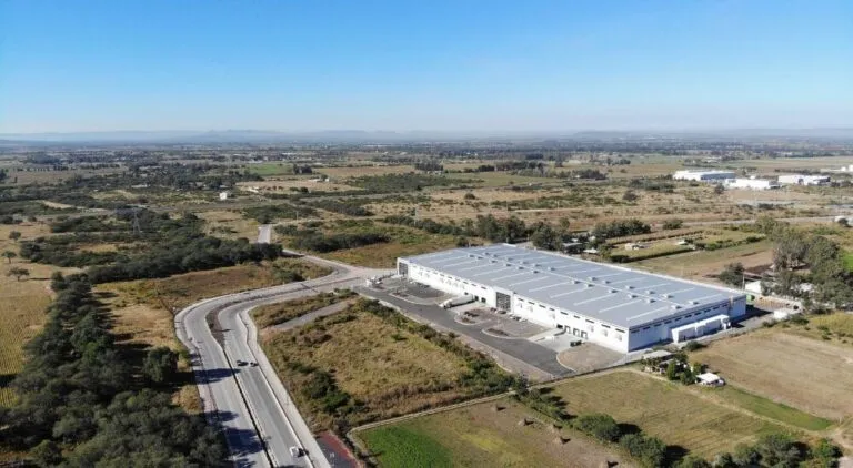 Aerial view of a large white-roofed warehouse complex bordered by a curved access road and open rural fields.