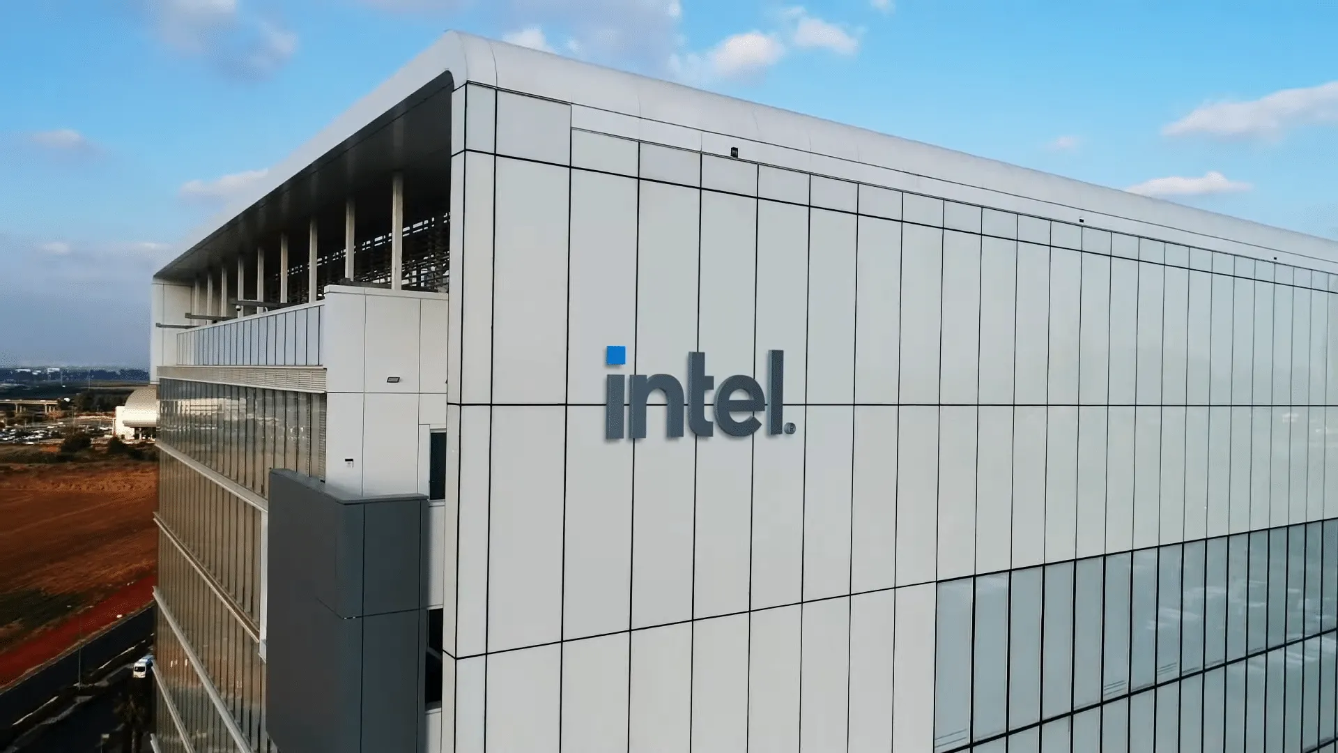 Exterior of an Intel office building with a white paneled facade, blue logo on the wall, and a clear blue sky above.
