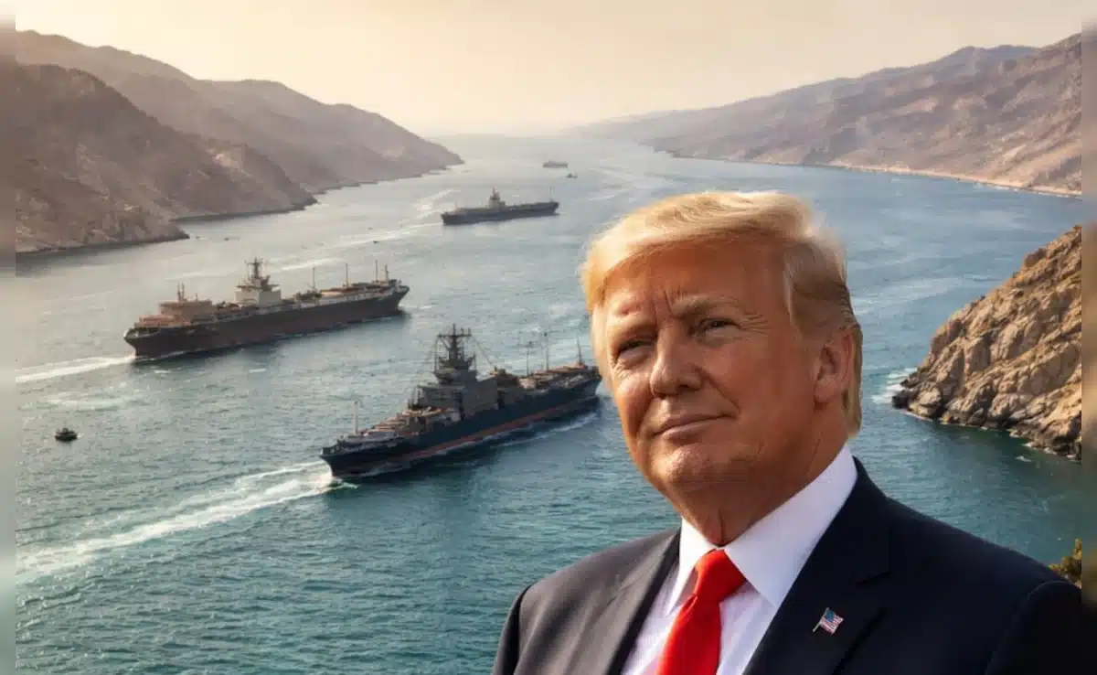 Man in a dark suit with a red tie posing in front of a harbor filled with large ships and rocky cliffs in the background.