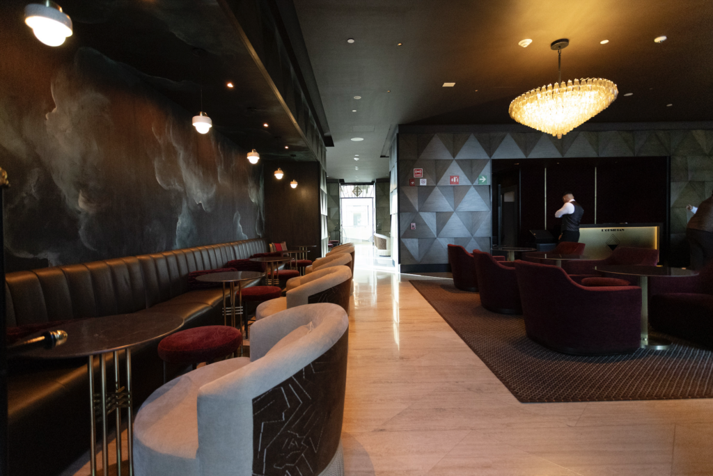 llobsidian_sofitel 1 - Petróleo y Energía Luxurious hotel lobby/lounge with black leather banquette seating, round tables, red stools, and a large chandelier overhead.