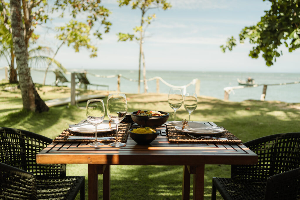 - Petróleo y Energía Outdoor seaside dining table set for four with wine glasses and bowls, overlooking the water.