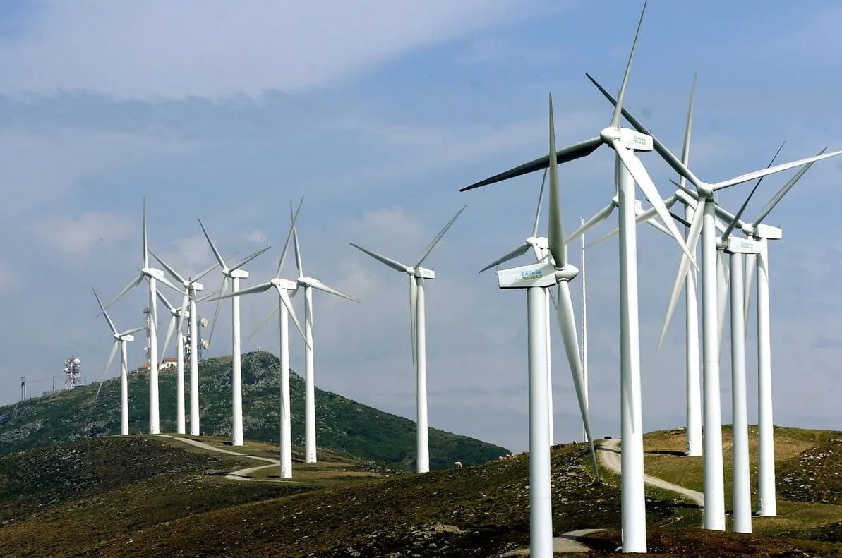 Row of white wind turbines on a hilly landscape against a blue sky, conveying clean energy generation.
