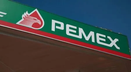 PEMEX gas station sign with green background, red stripe, and white logo flame motif against a blue sky