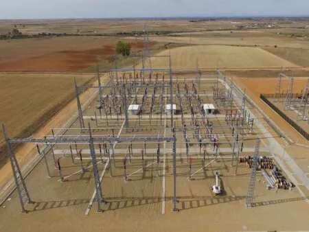 Aerial view of a large electrical substation with metal lattice towers, transformers, and wiring in a dry rural landscape.