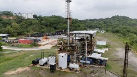 Industrial refinery facility with a tall smokestack, tanks and piping amid green hills