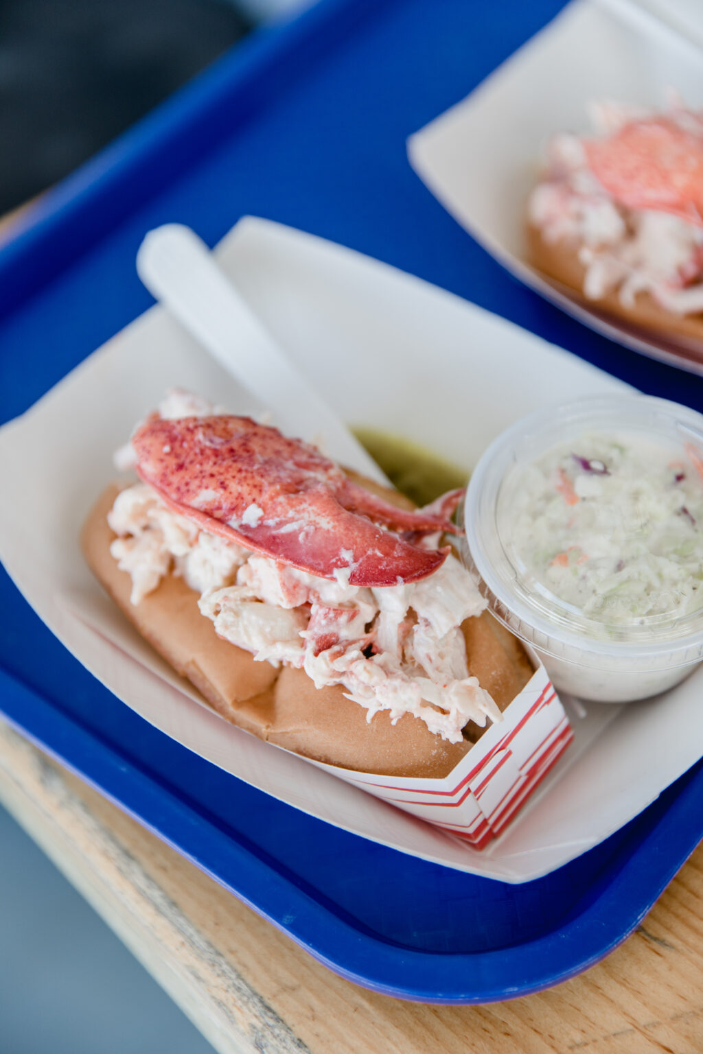 1 Maine - Lobster Roll 6 - Petróleo y Energía Lobster roll on a bun with lobster meat and mayo, served on a white tray with a blue background tray beneath.