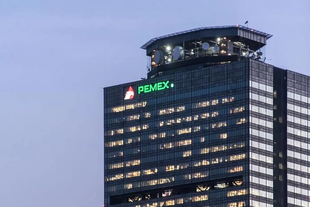 Tall glass skyscraper at dusk with a bright PEMEX logo on the top floors.