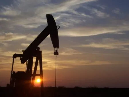 Silhouette of an oil pumpjack against a sunset sky on a flat horizon.