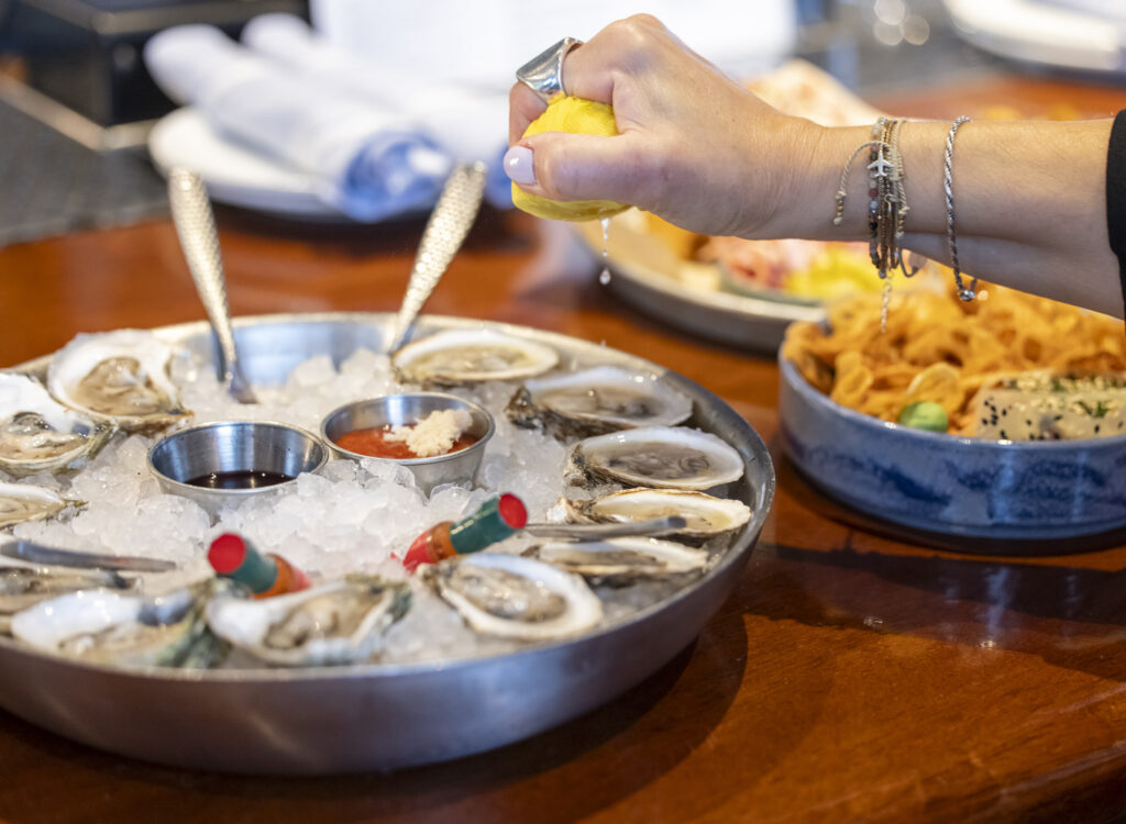 3 Boston Massachusetts - Comida 6 - Créditos a Kyle Klein - Petróleo y Energía Hand squeezing lemon over a tray of oysters on ice with dipping sauces and lemon wedge nearby.