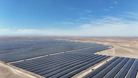 Utility-scale solar farm in a desert landscape under a clear blue sky, rows of dark solar panels stretching to the horizon.