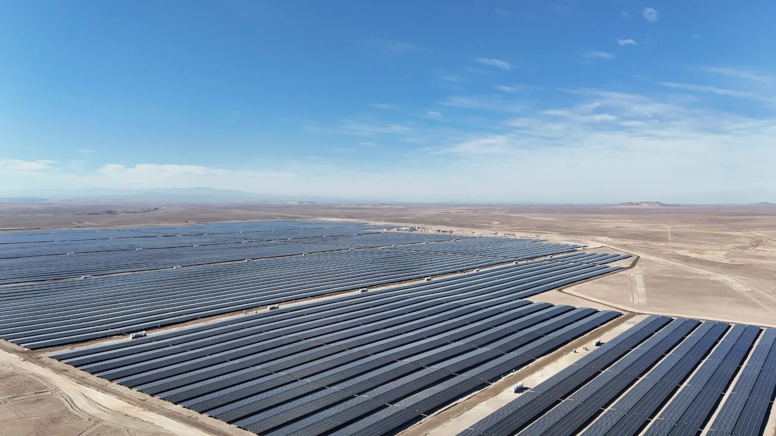 Utility-scale solar farm in a desert landscape under a clear blue sky, rows of dark solar panels stretching to the horizon.