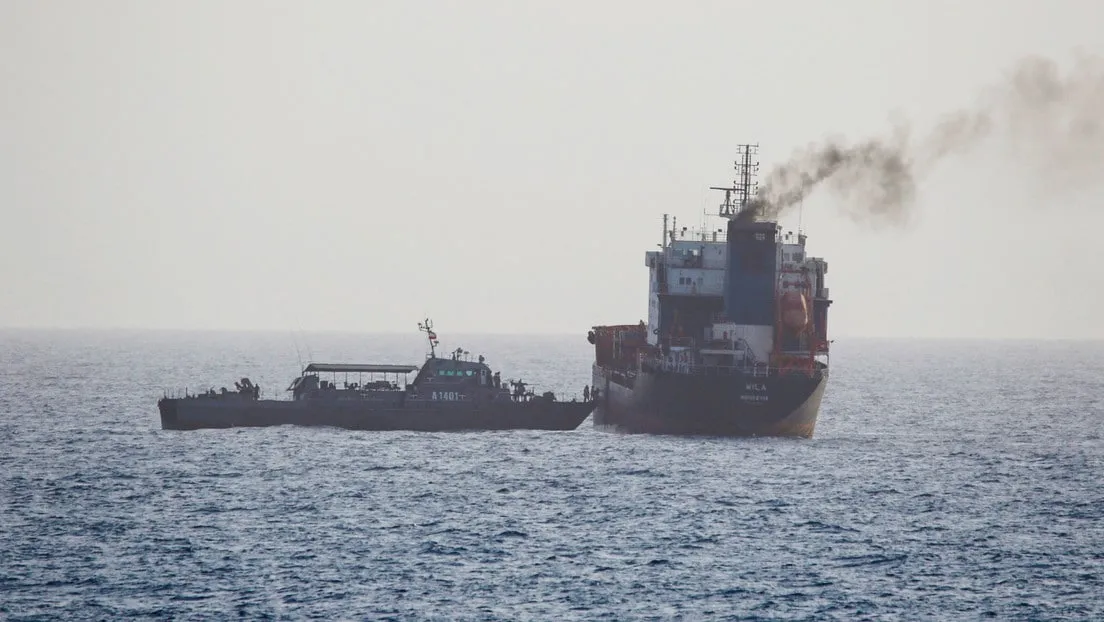 Small patrol/tug boat beside a large container ship at sea, with dark smoke from the ship's funnel.