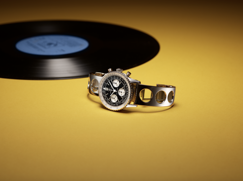 BREITLING JAZZ 2 - Petróleo y Energía Stainless steel chronograph wristwatch with a black dial resting on a yellow surface, vinyl record blurred in the background.
