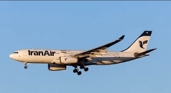 IranAir passenger jet with landing gear down, flying against a clear blue sky.
