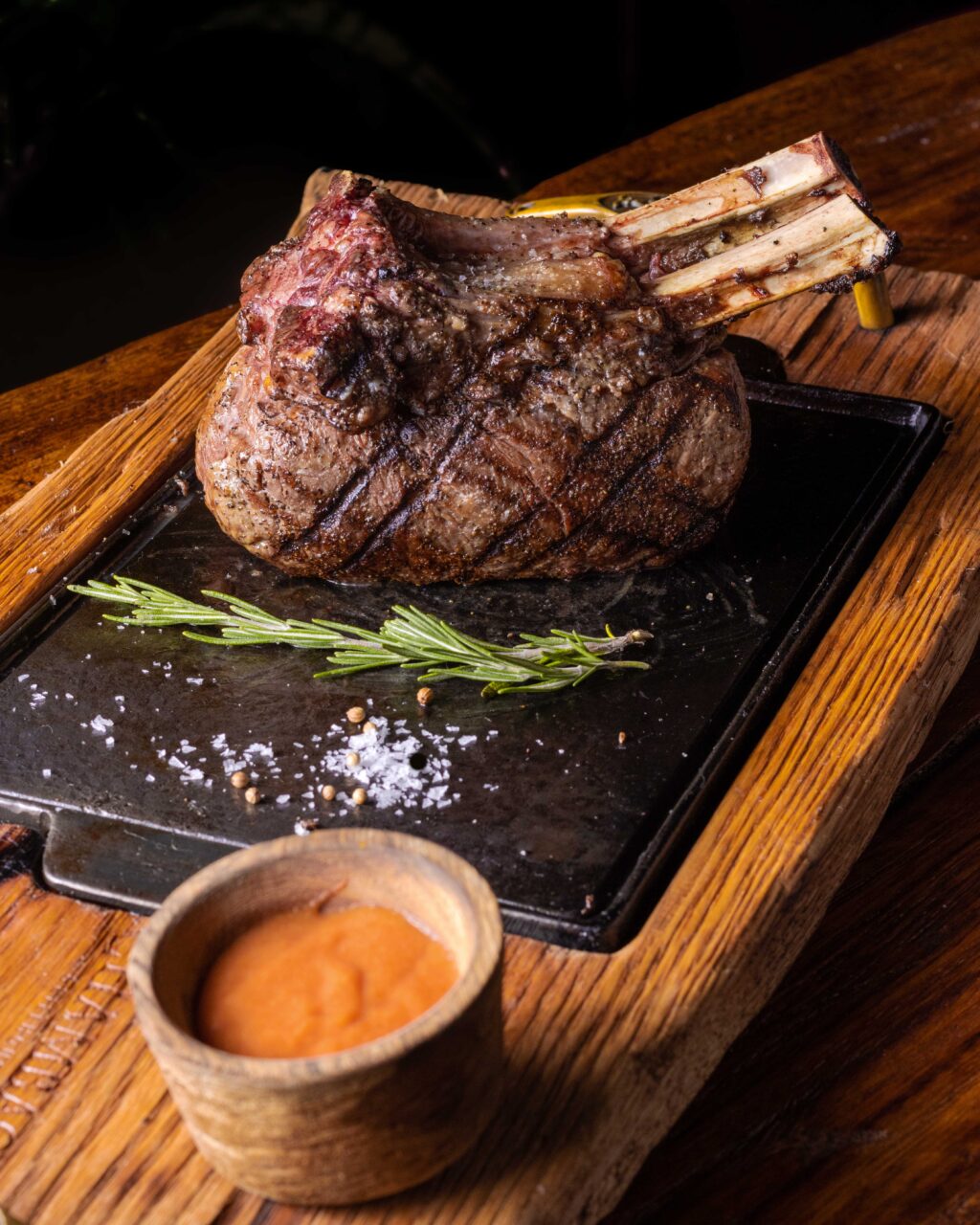 ChAMd_10Octubre23-4576 - Petróleo y Energía Beef rib roast with exposed rib bones on a wooden board, garnished with rosemary, salt, and pepper.