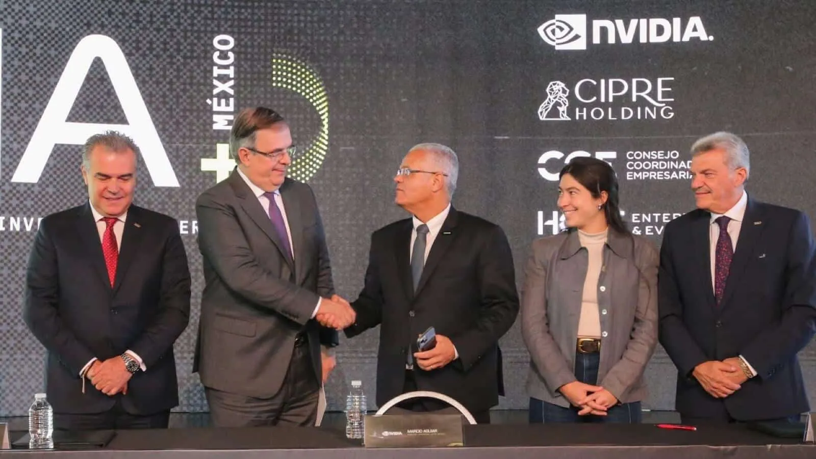 Five professionals in business attire stand behind a conference table as two men in the center shake hands during a formal signing event, with water bottles on the table and a dark backdrop displaying corporate logos including NVIDIA and CIPRE Holding.