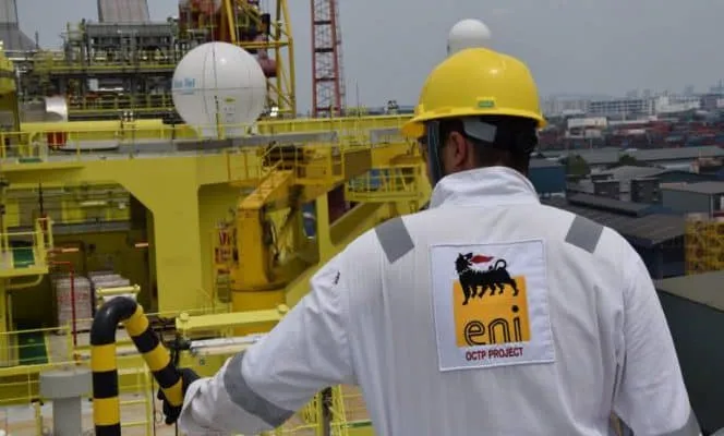 Worker in white coveralls and a yellow helmet on an offshore industrial platform; ENI OCTP Project logo visible on back.