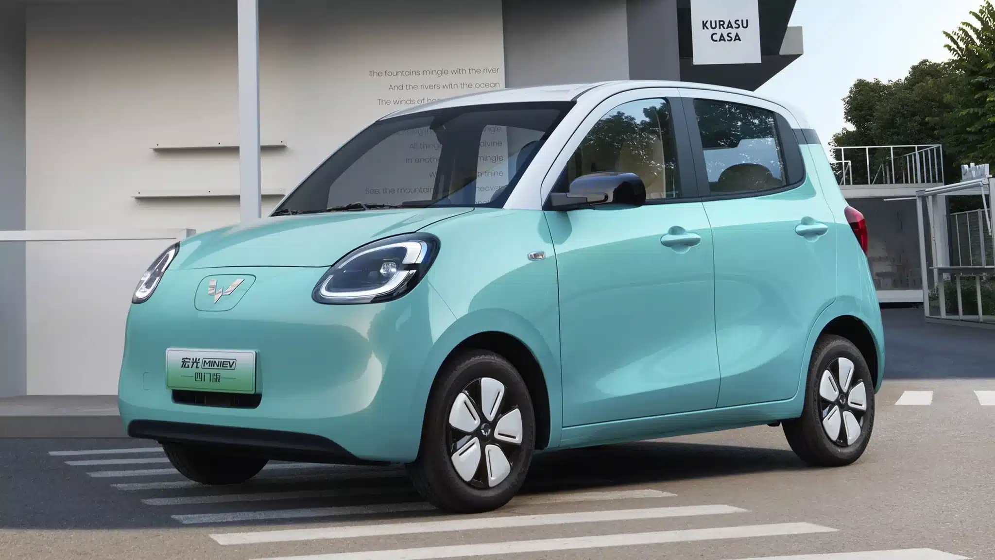 Mint teal compact hatchback parked in a space near a modern building, front-left angle showing its rounded headlights and dual-tone roof.