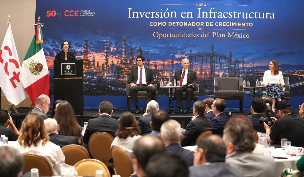 HRP9nWPbsAA8gCj - Petróleo y Energía Woman at a podium delivering a speech while two men sit on the panel and a woman sits to the right on a stage backdrop, flags present.