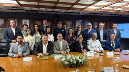 Group of diverse professionals posing for a group photo in a conference room around a long wooden table with nameplates and a flower centerpiece.