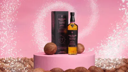 The Macallan Harmony Collection whisky bottle with its box on a pink pedestal, surrounded by coconuts.