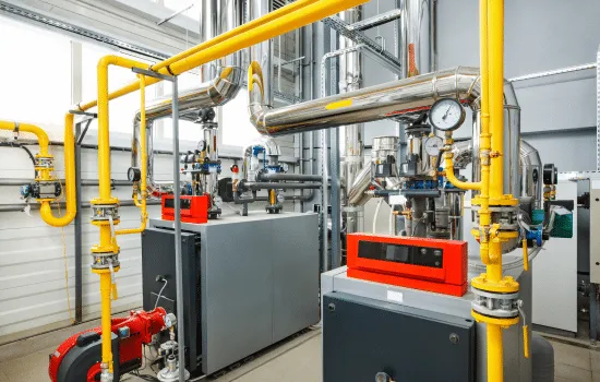 Industrial boiler room with yellow gas pipes, gauges, and gray control panels.
