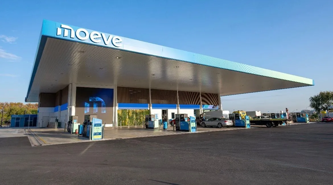 Gasoline station under a large blue canopy with multiple fuel pumps and cars refueling.