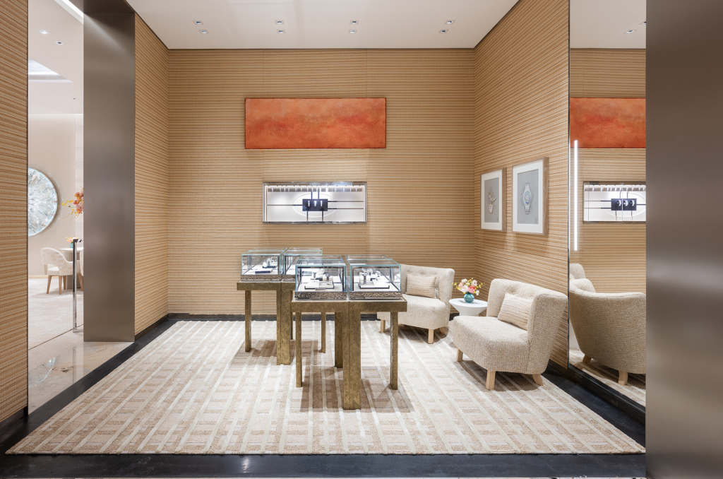 NUEV BOUTIQUE TIFFANY 2026-09-24 a las 44327 pm - Petróleo y Energía Boutique showroom with striped beige walls, a rectangular orange art piece, and glass jewelry displays on gold tables surrounded by beige seating.