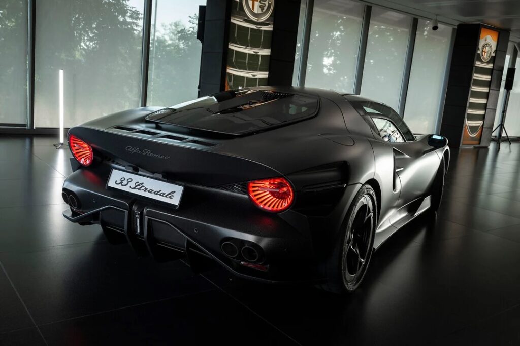 Rear three-quarter view of a matte black Alfa Romeo 33 Stradale on display in a showroom, with red taillights and a'33 Stradale' plate.]","Matte black Alfa Romeo 33 Stradale sports car in a showroom, rear view with quad exhausts and a prominent diffuser.]","Alfa Romeo 33 Stradale concept car on showroom floor, rear view showing red circular taillights and '33 Stradale' plate.]","Showroom scene featuring a black Alfa Romeo 33 Stradale from the rear, highlighting the sporty design and tail lights.]
