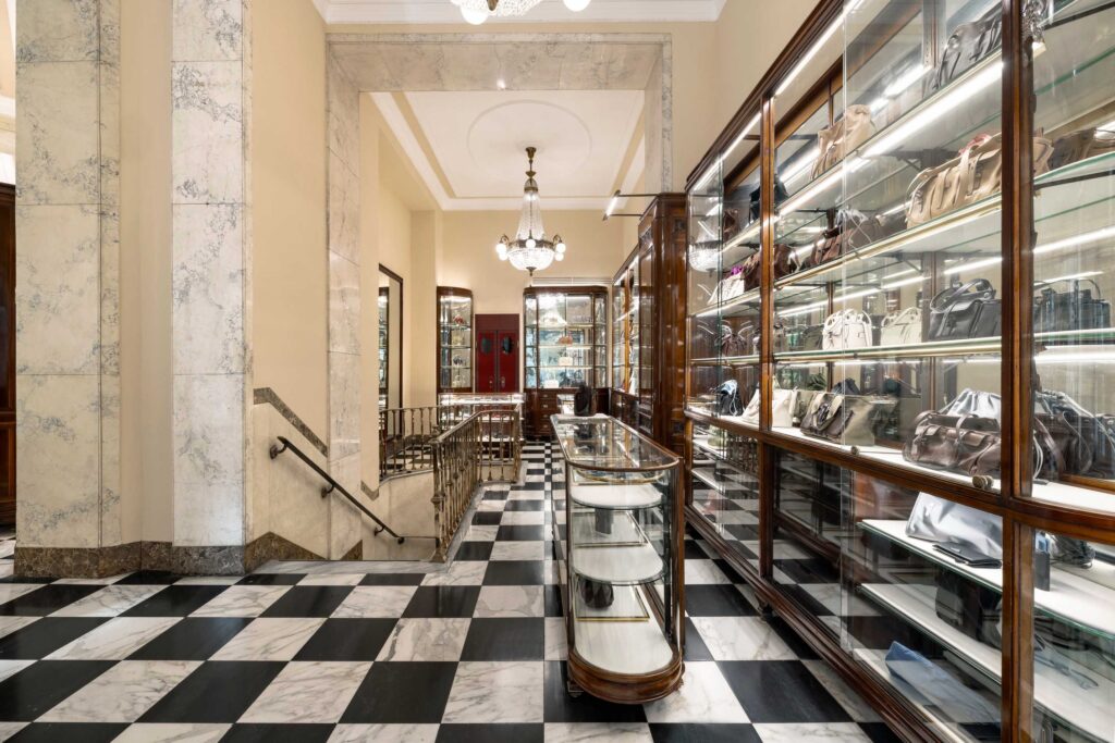 Prada Donna_Prada Galleria Vittorio Emanuele II - Petróleo y Energía Luxurious handbag boutique interior with glass display cases along the right and a black-and-white checkered marble floor.