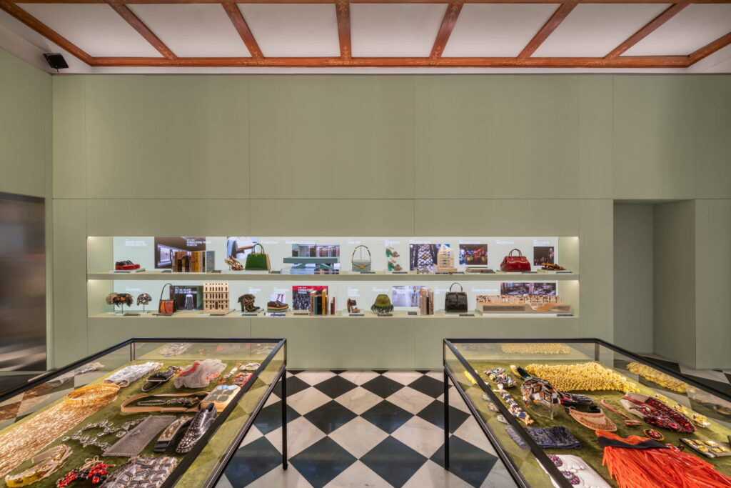 Pradasphere_Prada Galleria Vittorio Emanuele II_02 - Petróleo y Energía Display showcases with assorted handbags, jewelry, and accessories along glass display counters in a green-walled boutique.